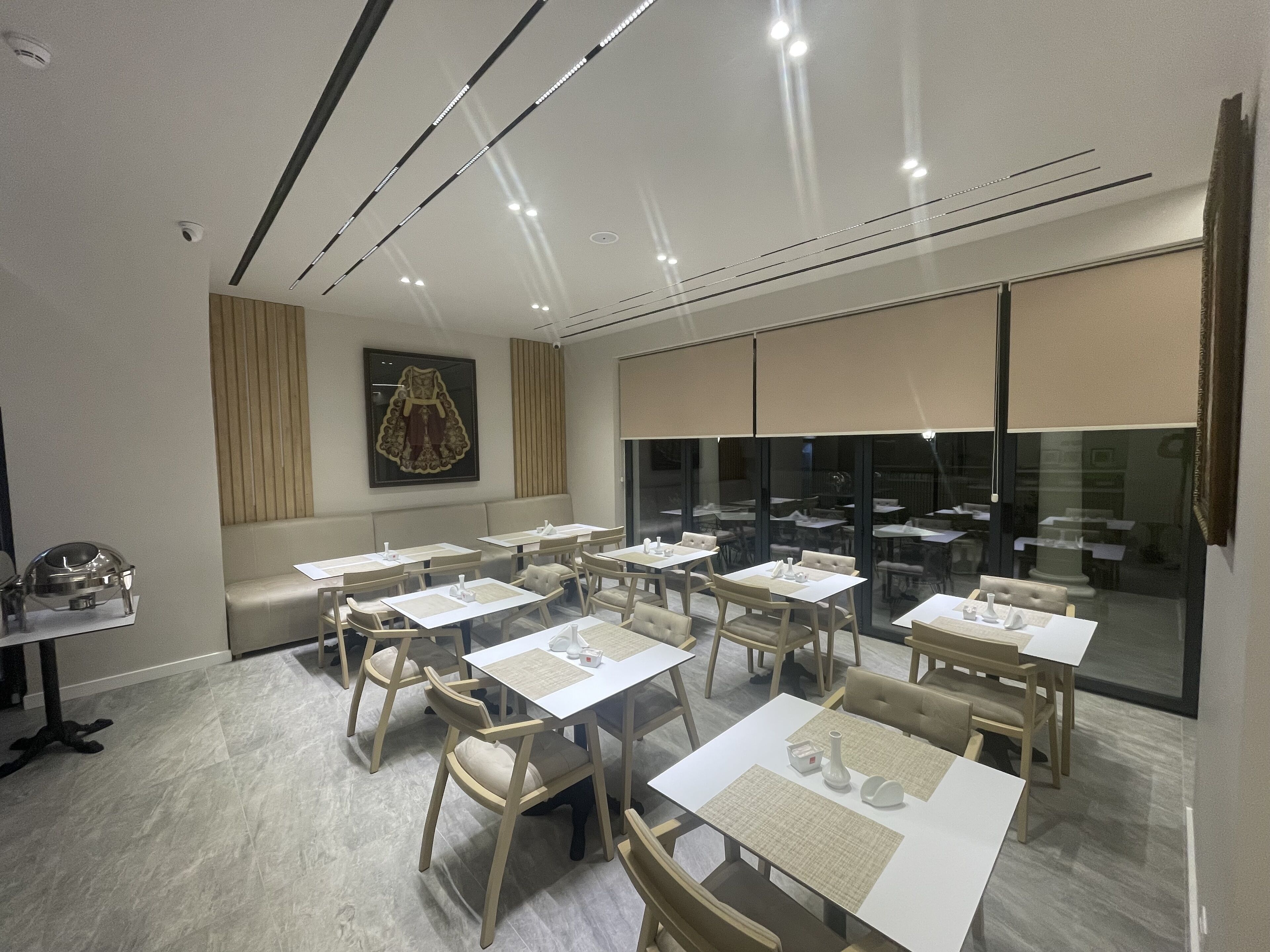 A modern dining area with multiple tables and chairs, a large window with a view, and a wall-mounted artwork.