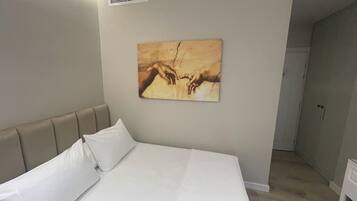 A hotel room with a large bed, a headboard, a wall-mounted artwork, and a door leading to another room.