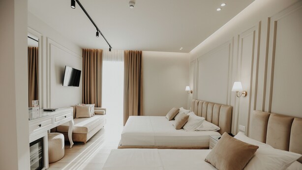 Una habitación de hotel moderna con una cama grande, un escritorio con televisor de pantalla plana y una zona de estar con sofá y reposapiés.