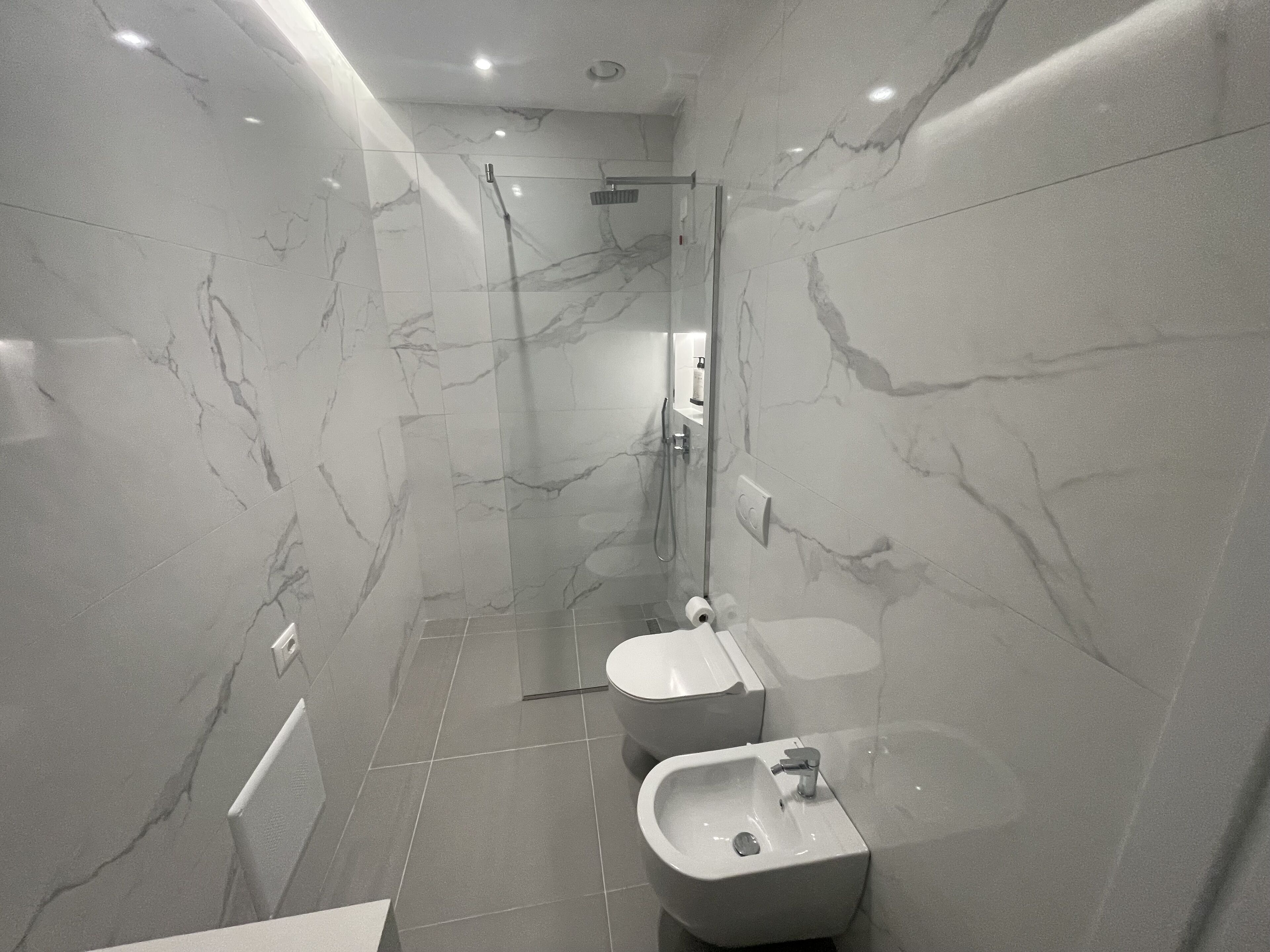A modern bathroom with marble walls, a glass-enclosed shower, and a pedestal sink.