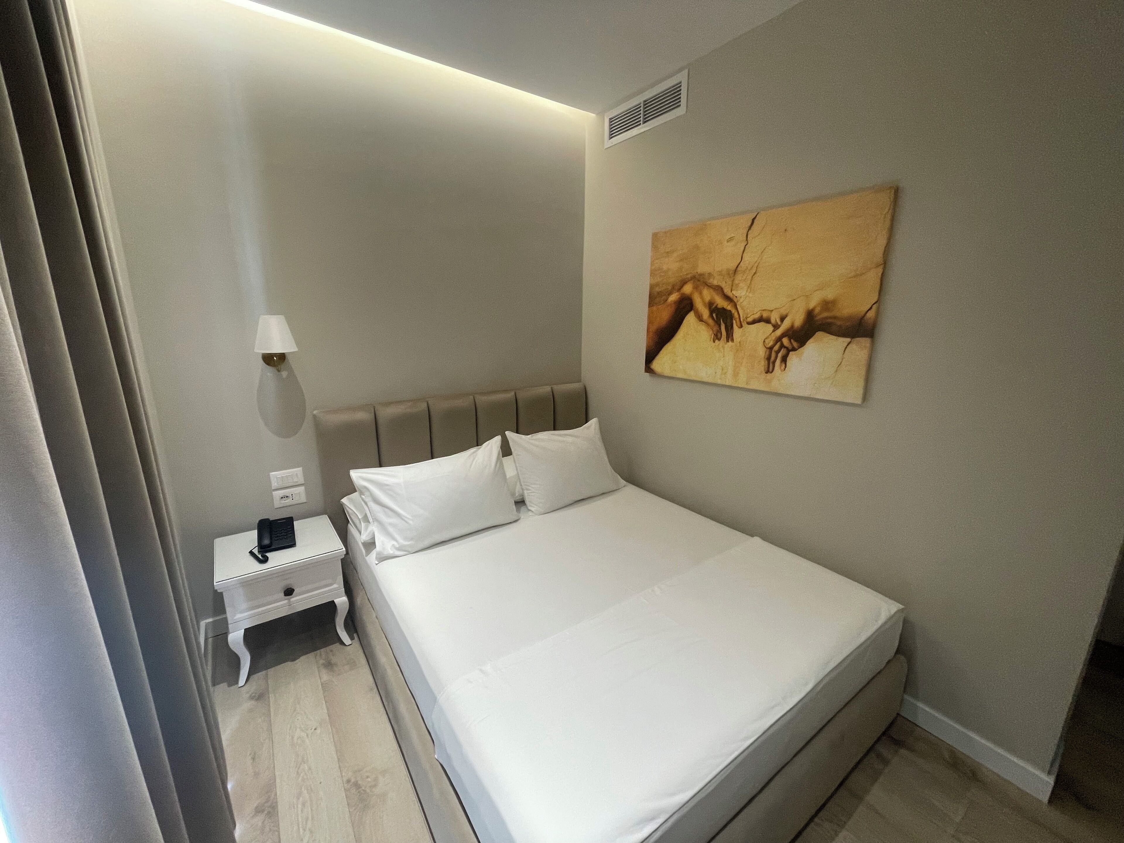 A hotel room with a bed, a nightstand, a lamp, and a painting on the wall.