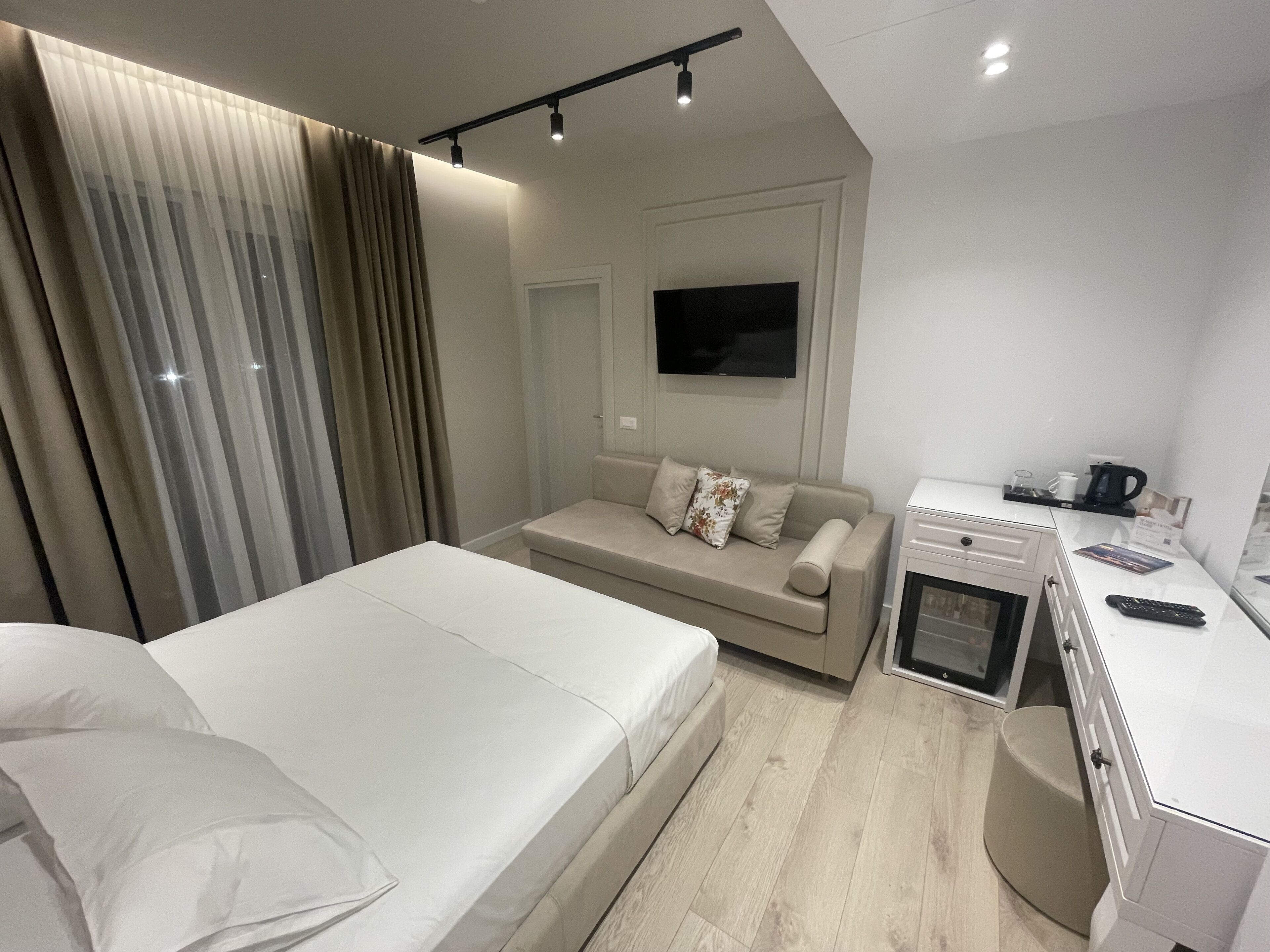 A modern hotel room with a bed, a sofa, a desk with a coffee machine, and a TV.