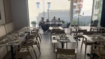 Um restaurante com várias mesas e cadeiras, uma janela grande e vista para edifícios.