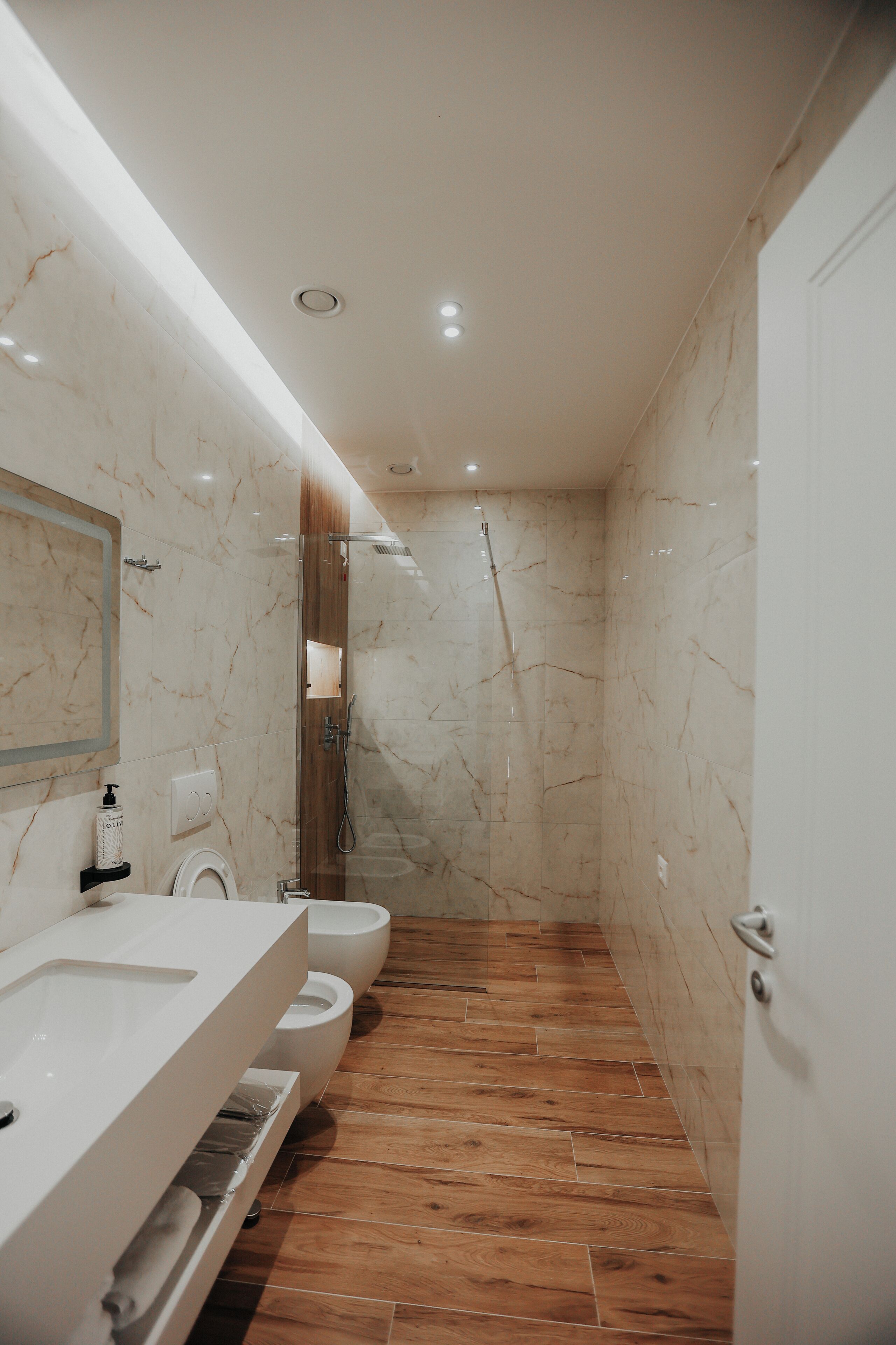 Un baño moderno con tocador de mármol, ducha y piso de madera.