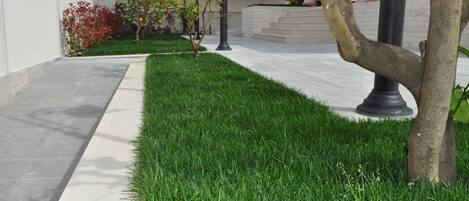 A well-maintained grassy area with a paved walkway, a street lamp, and a tree.