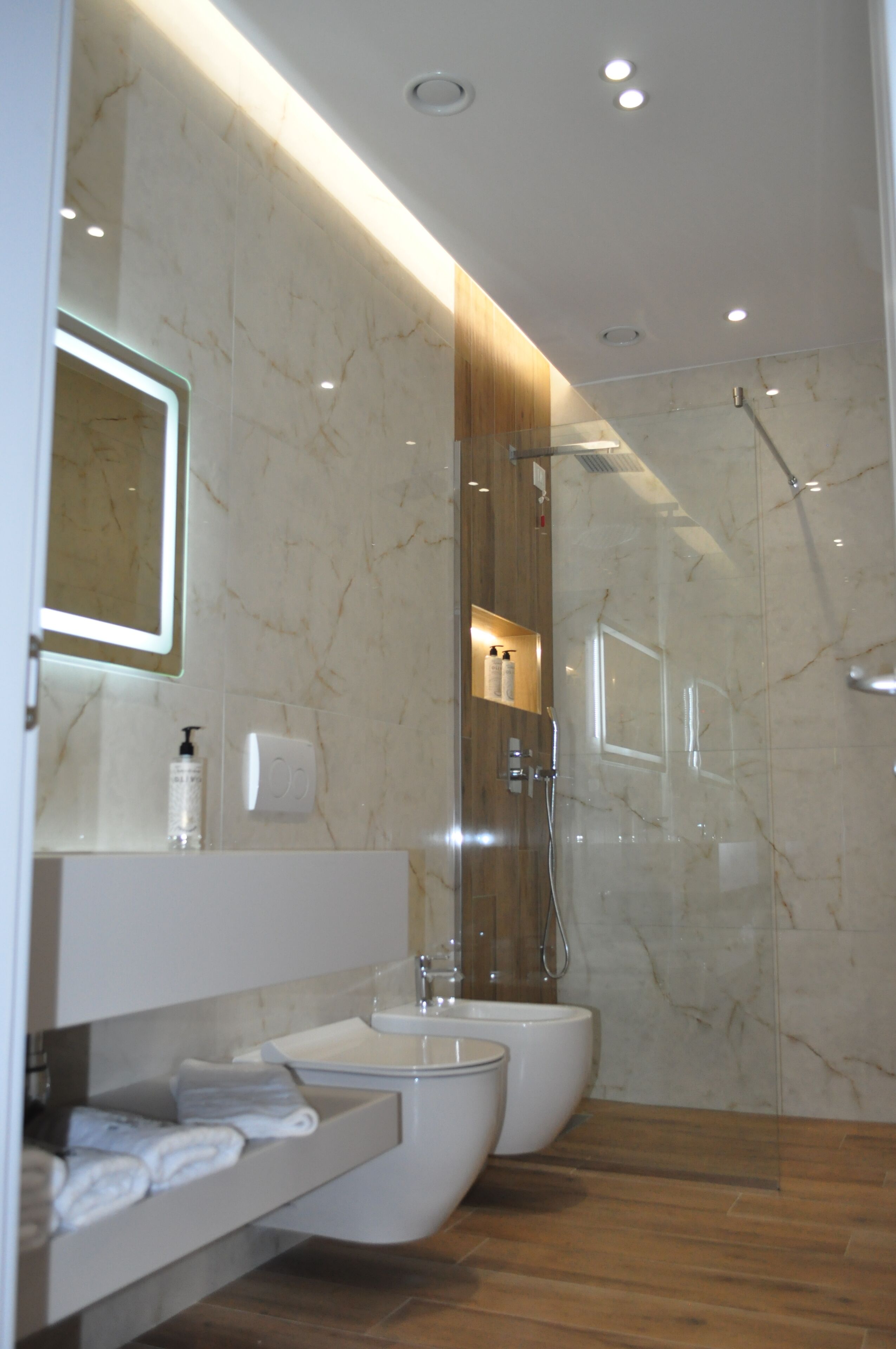 Un baño moderno con ducha envuelta en vidrio, tocador con espejo y dos inodoros.