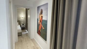 A hallway with a painting of a woman, a bed, and a nightstand.