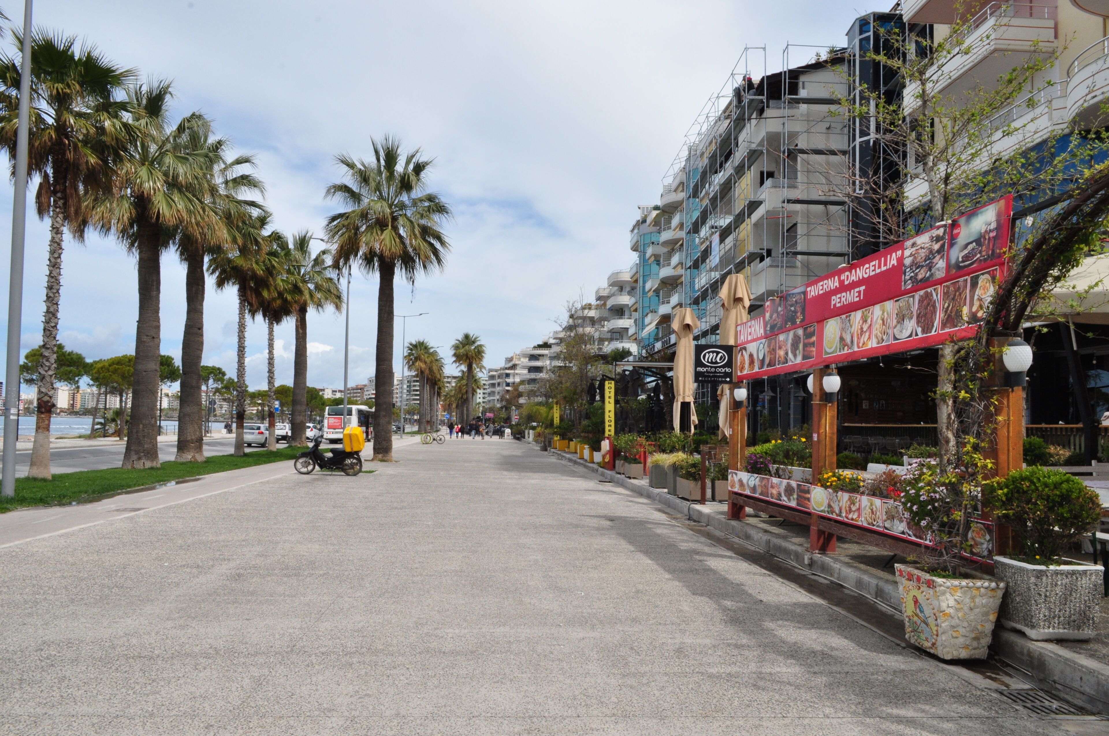 A street lined with palm trees and a restaurant named "Taverna 'D'Angellia' Permet".