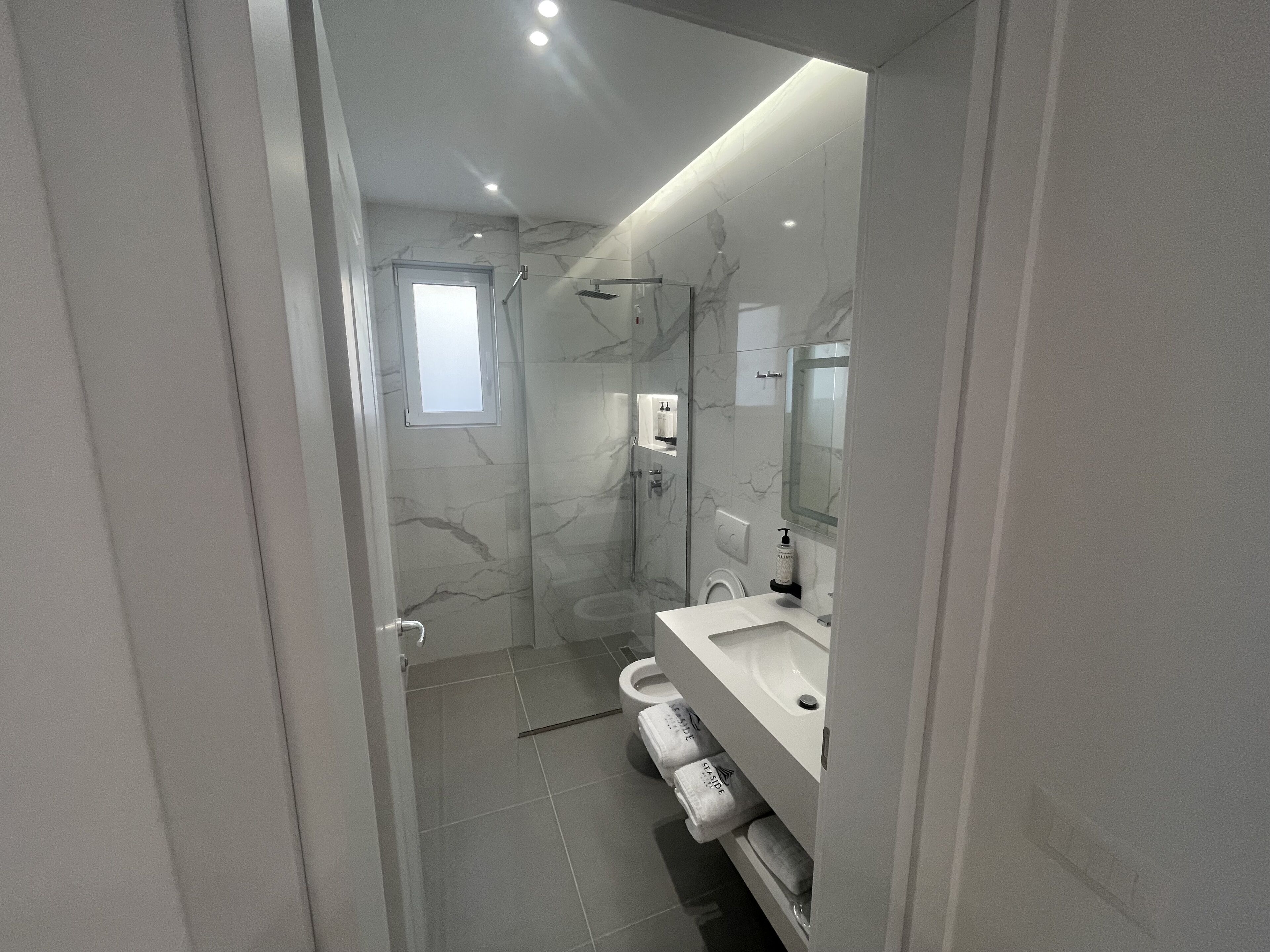 A modern bathroom with a glass-enclosed shower, a white sink, and a large mirror.