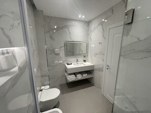 A modern bathroom with a marble backsplash, a built-in sink, a toilet, and a glass shower enclosure.