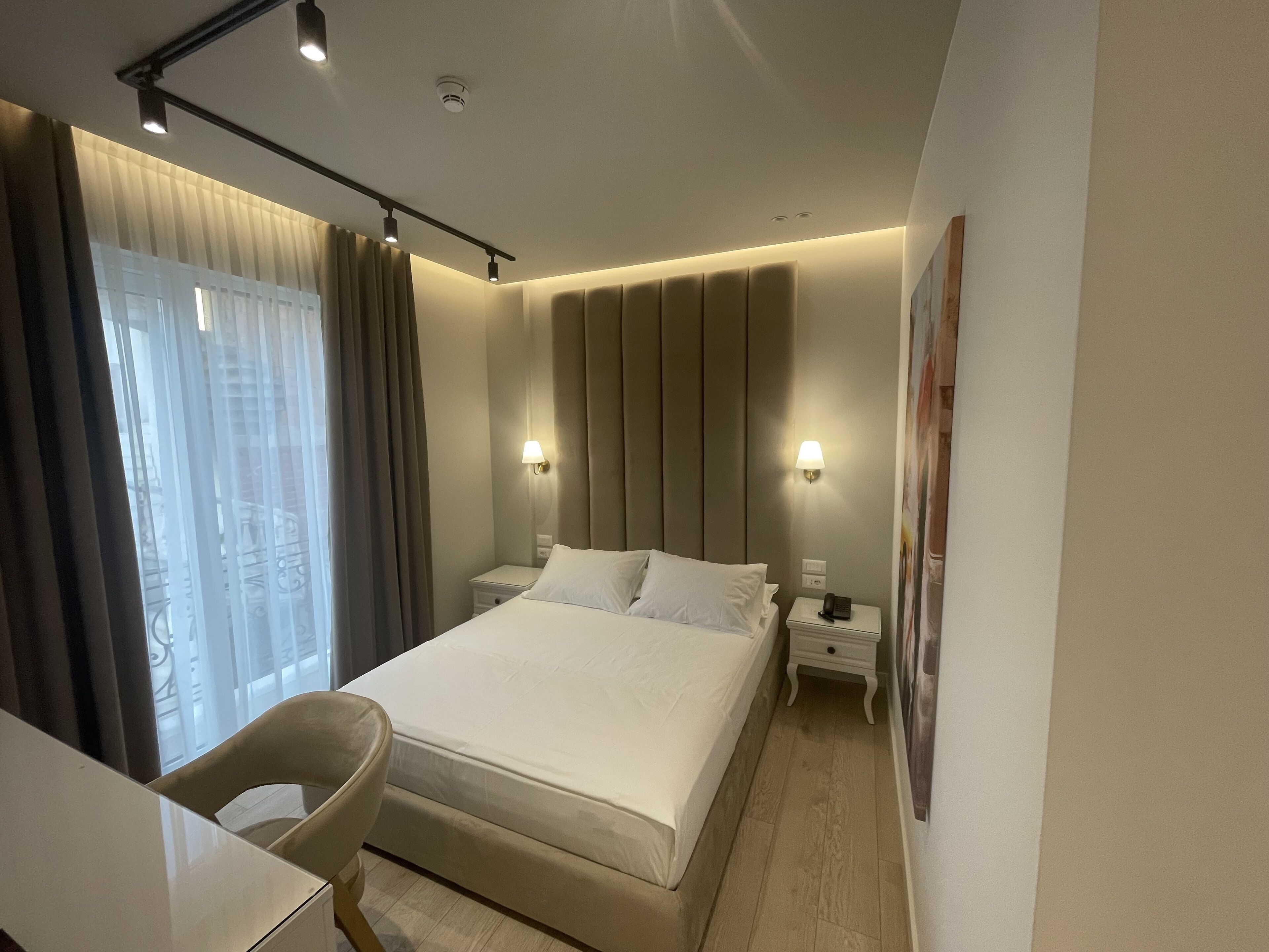 A modern hotel room with a large bed, bedside tables, a desk, and a chair.