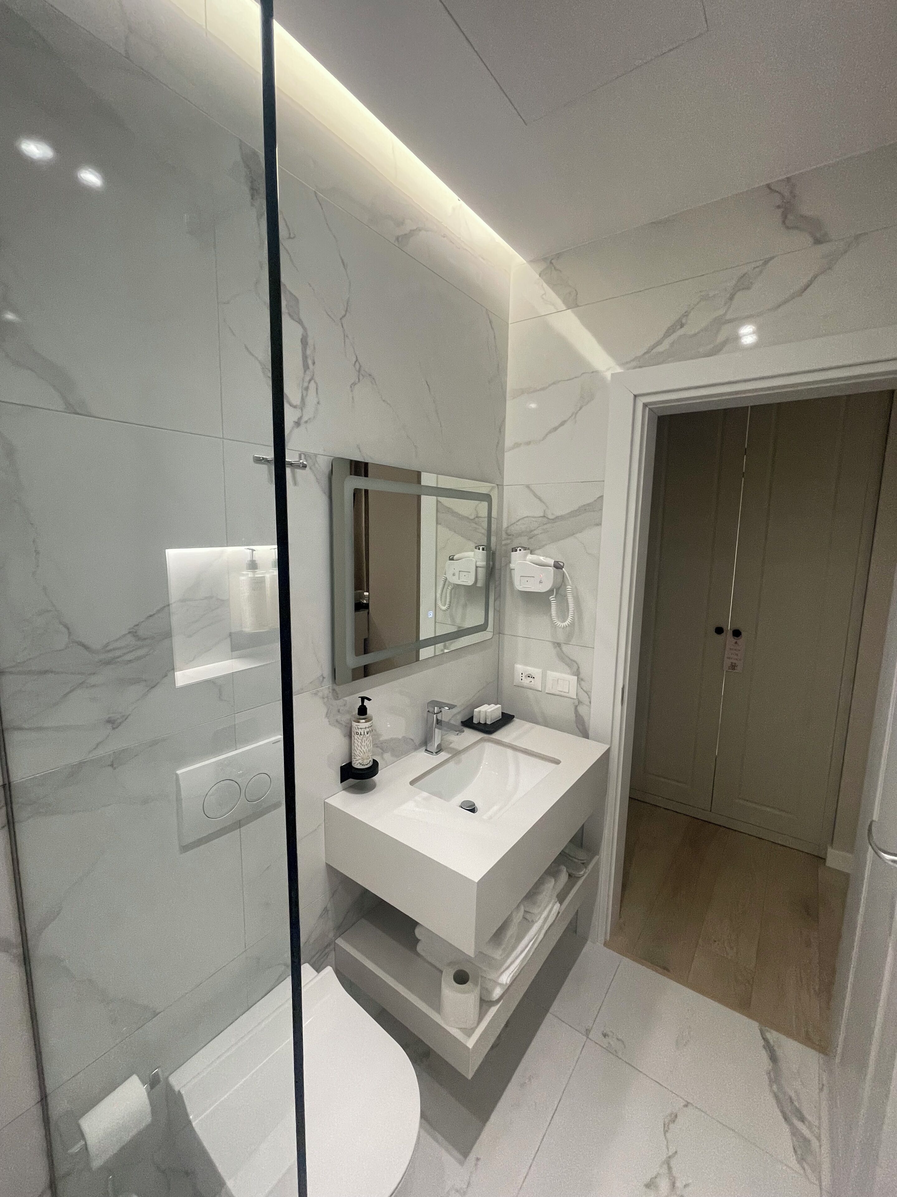 A modern bathroom with a glass-enclosed shower, a large mirror, a white sink, and a toilet.