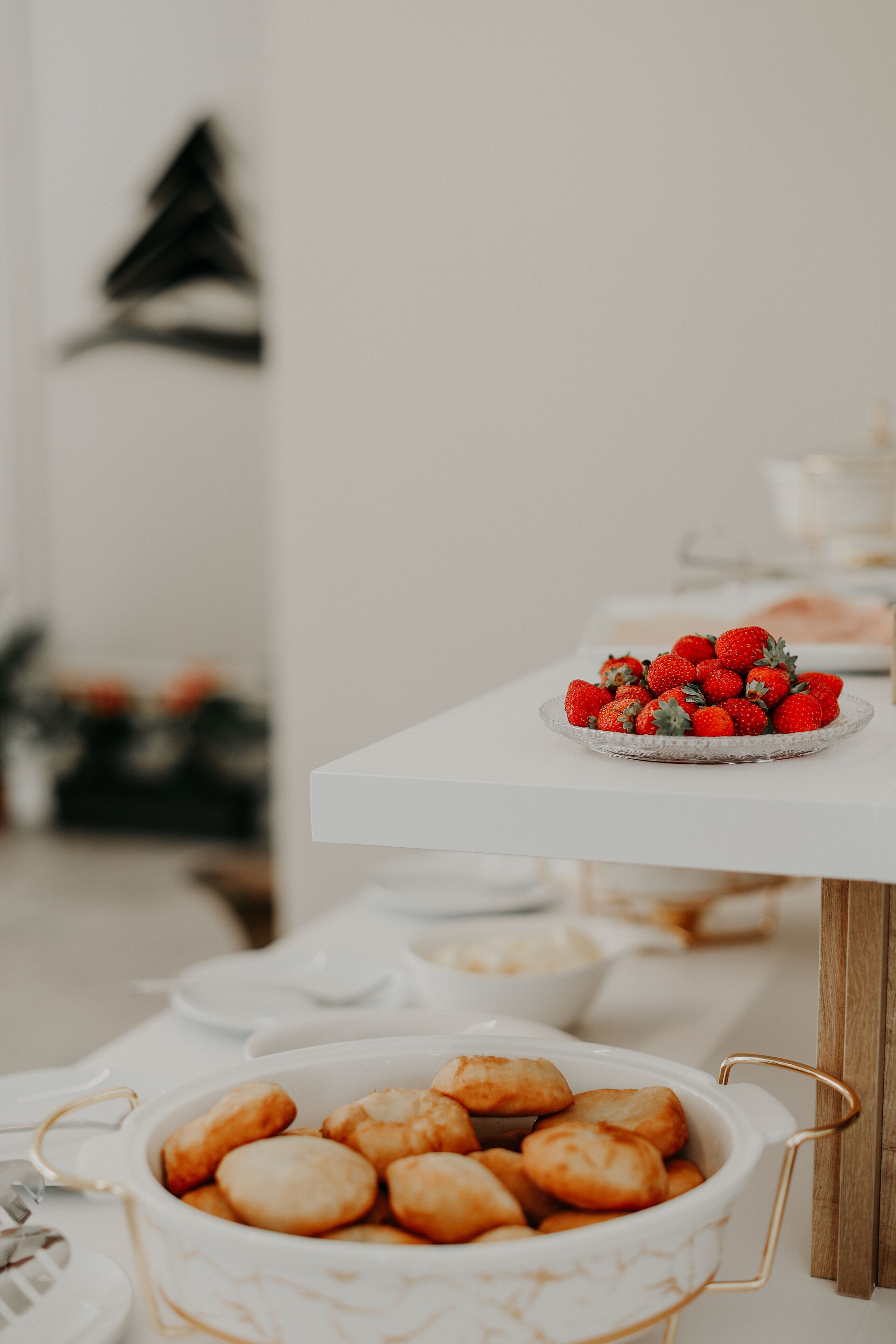 A table with a white plate of strawberries and a white bowl of cookies.