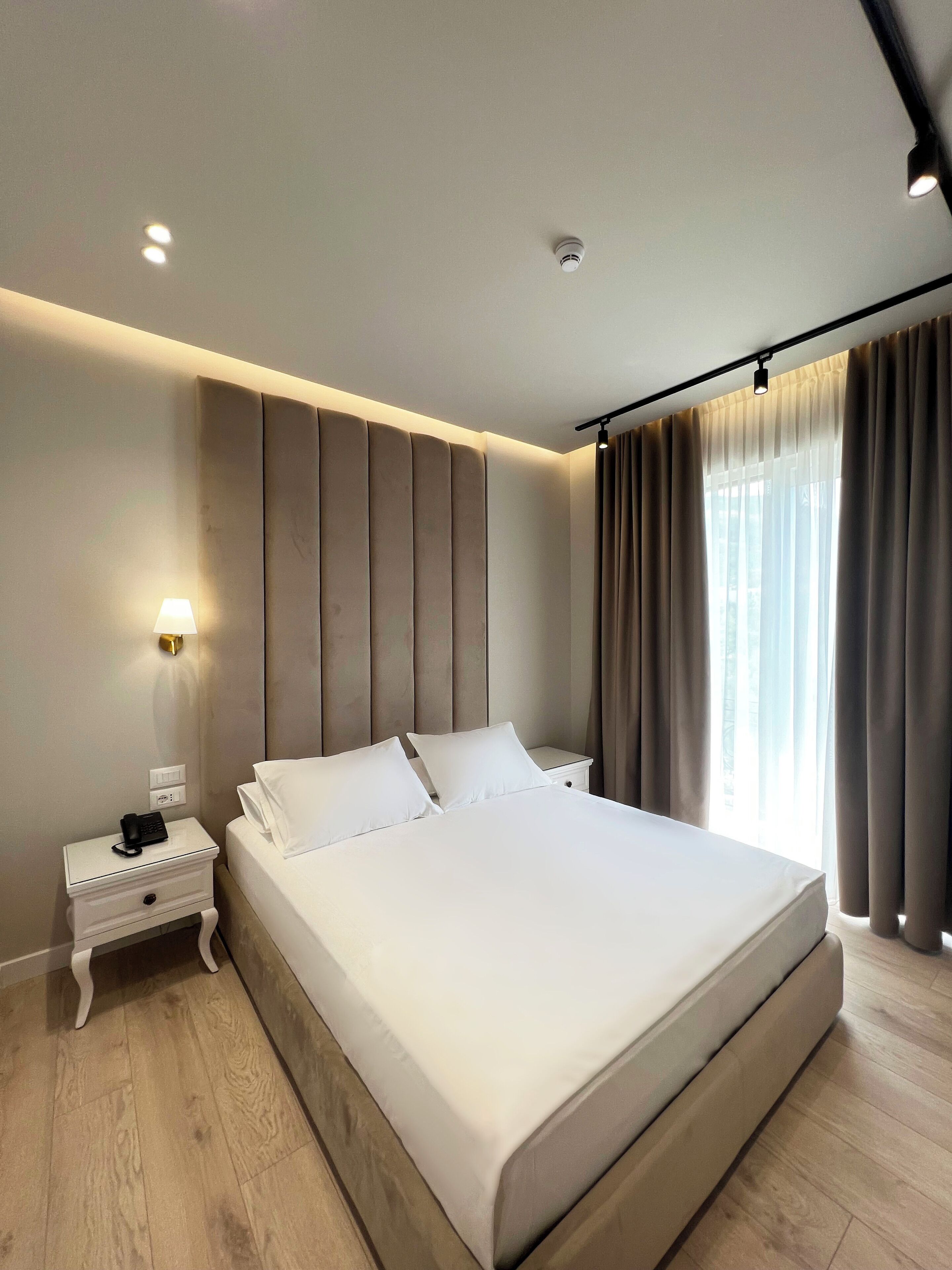 A modern hotel room with a large bed, a bedside table with a lamp, a wall-mounted air purifier, and a window with curtains.