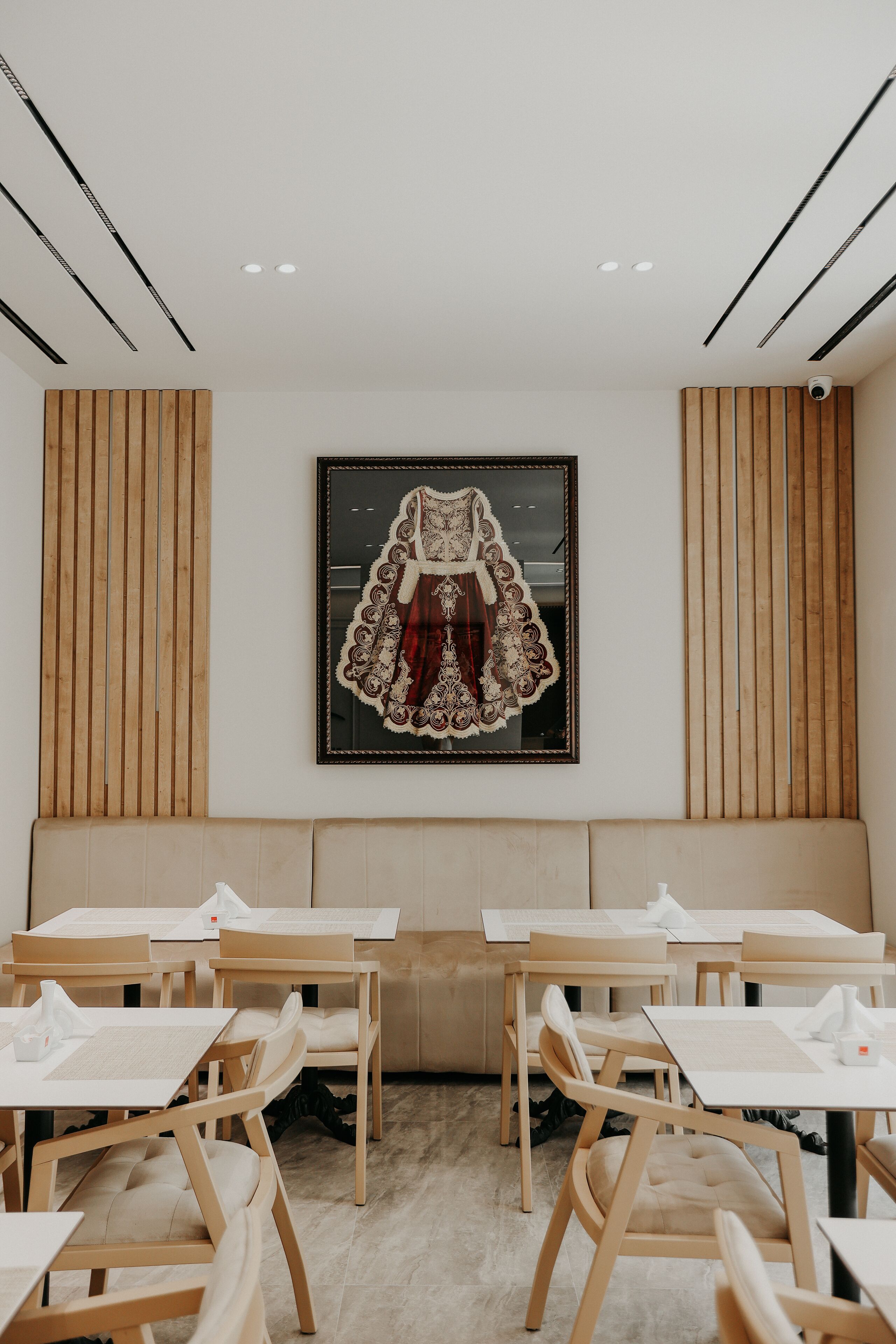 A dining area with wooden tables and chairs, a large framed artwork on the wall, and a wooden slat wall design.