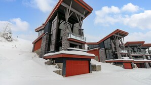 A modern ski lodge with a red garage door, stone pillars, and a sloped roof.