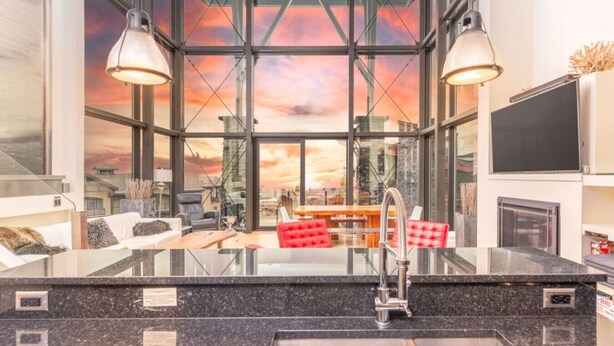 A modern kitchen with a large island, a red upholstered chair, and a view of the city through large windows.