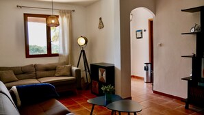 En stue med en sofa, et lille bord, en gulvlampe og udsigt gennem en buet åbning til et andet rum.