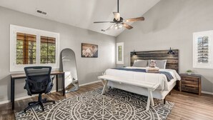 A bedroom with a bed, desk, chair, and a ceiling fan.