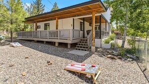 A two-story cabin with a covered porch, a small deck, and a gravel driveway.