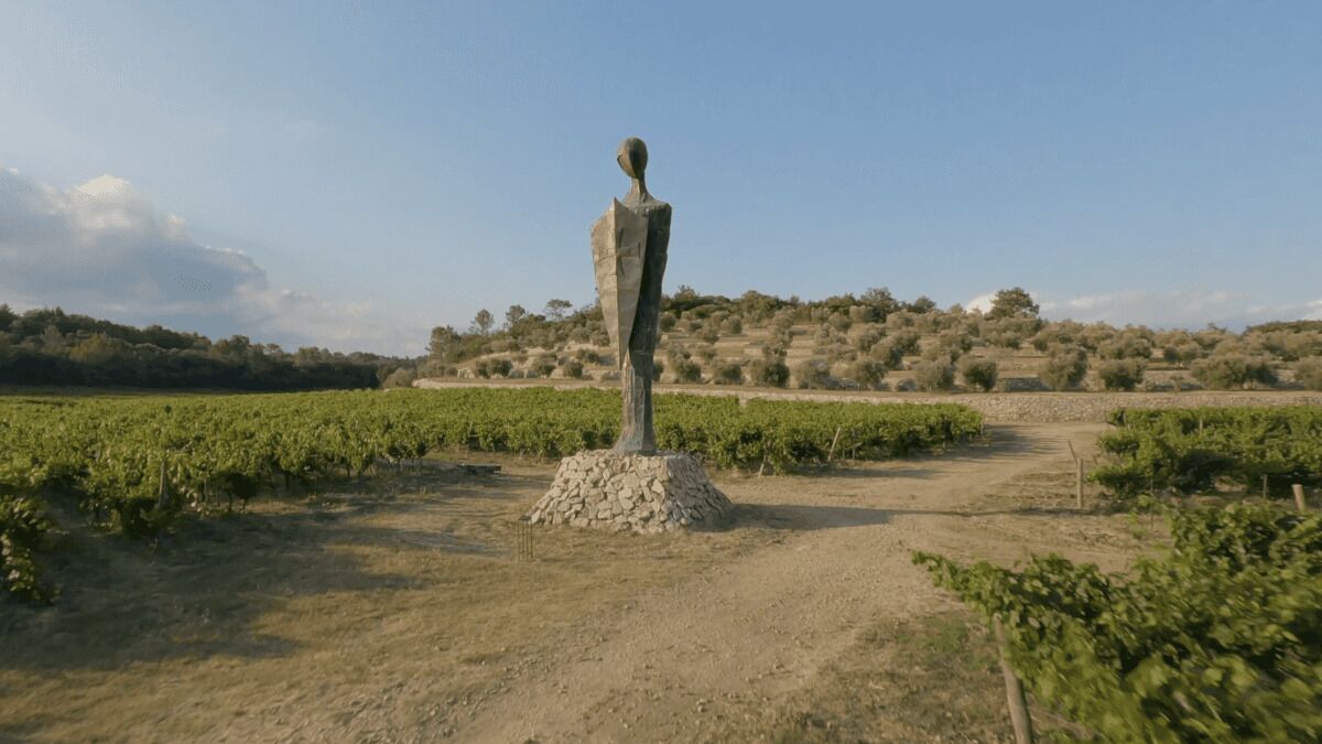 Un vignoble avec des rangées de vignes et une statue de pierre au centre.
