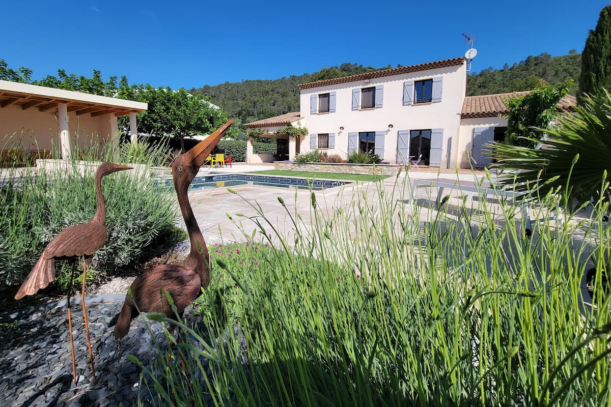 Una villa con piscina, mobiliario de exterior y un jardín con hierbas altas.