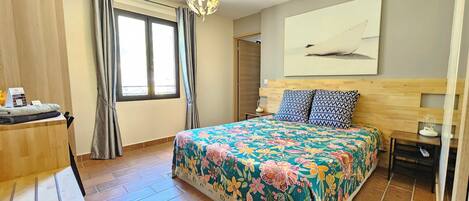 Een slaapkamer met een bloemenprint bedsprei, een houten hoofdbord, een nachtkastje en een raam met gordijnen.