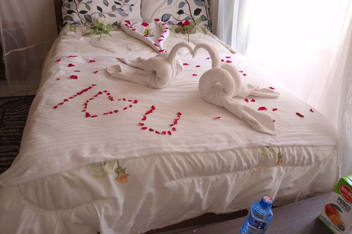 A bed with a heart-shaped arrangement of rose petals and towels shaped like swans, with the word "love" spelled out in rose petals.