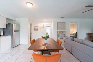 Una cocina moderna con refrigerador integrado, una mesa de comedor con sillas naranjas y un sofá gris en la sala.