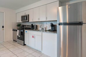 Una cocina moderna con electrodomésticos de acero inoxidable, armarios blancos y piso de baldosas.