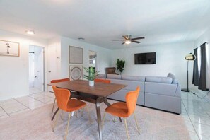 A modern living room with a dining area, a ceiling fan, and a grey sofa.