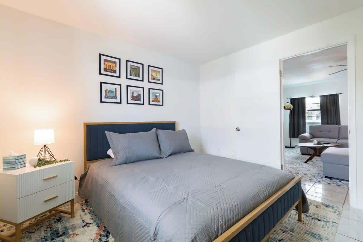 A bedroom with a bed, bedside table, lamp, and wall art.