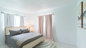 Une chambre à coucher avec un lit, des rideaux, une lampe et un tableau au mur.