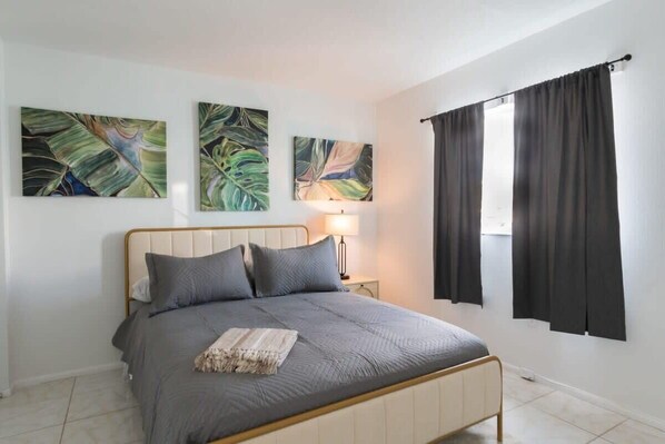 Un dormitorio con una cama, una mesita de noche, una lámpara y tres cuadros colgados en la pared.