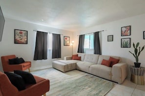 Ein Wohnzimmer mit Ecksofa, einem roten Sessel, einer Stehlampe und einer Topfpflanze.