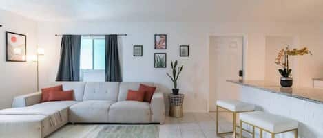 Una sala moderna con un sofá modular, una mesa de centro y una zona de bar con taburetes.