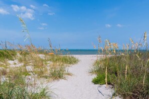 Ein Sandweg am Strand, umgeben von grasbewachsenen Flächen, der zum Meer führt.
