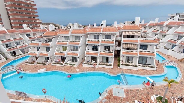 A resort with multiple white buildings, a central swimming pool, and a view of the ocean. - Las Floritas 22 - One Bed ground floor with pool (Playa de la Américas)