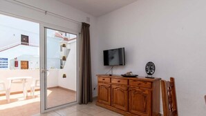 A room with a sliding glass door leading to a balcony, a wooden cabinet with a flat-screen TV, and a dining table with chairs. - Las Floritas 22 - One Bed ground floor with pool (Playa de la Américas)