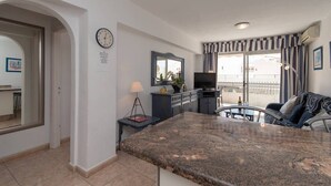 A modern kitchen with granite countertops, a dining area with a sofa, and a balcony with a view. - Santa Maria 67 - Two Bed (Costa Adeje)