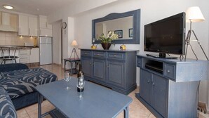 A modern living room with a sofa, a coffee table with wine glasses, a TV, and a cabinet with a mirror above it. - Santa Maria 67 - Two Bed (Costa Adeje)