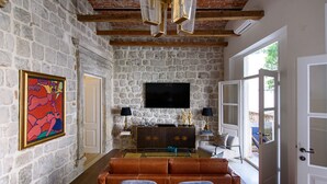 A stone-walled room with a wooden ceiling, a flat-screen TV, a sofa, and a dining table.