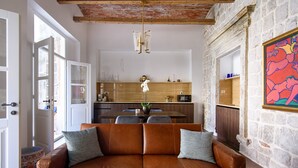 A cozy living room with a brown leather sofa, a dining table, and a kitchen in the background.