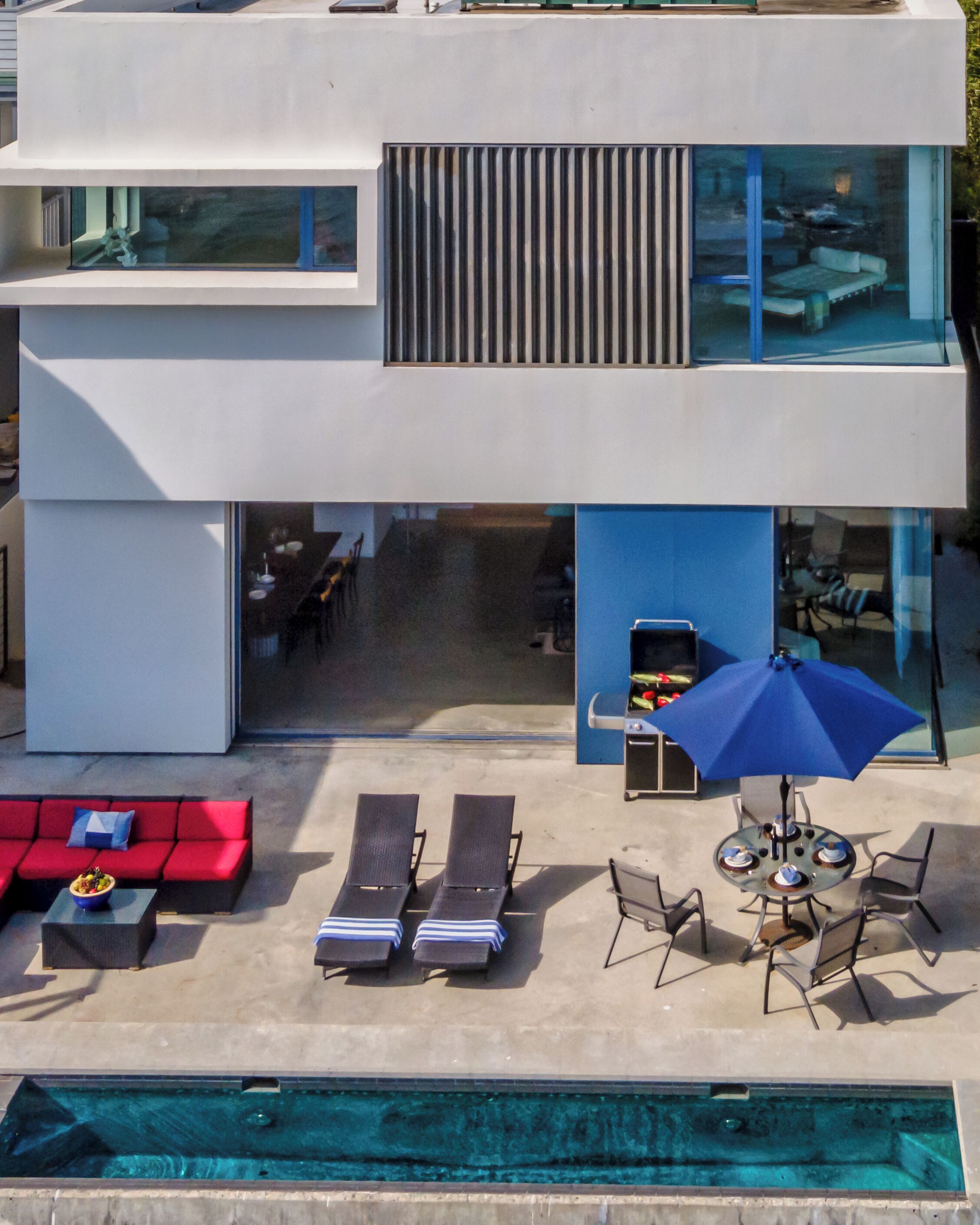 A modern two-story house with a pool, outdoor seating, and a dining area.