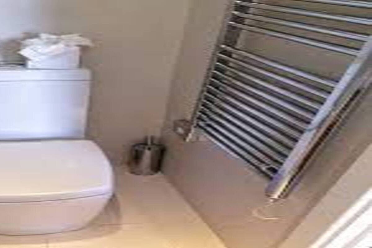 A small, compact bathroom with a toilet, a towel rack, and a trash can.