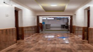Un pasillo con paneles de madera, suelo de baldosas y una puerta al final que da a una habitación con cama y ventana.