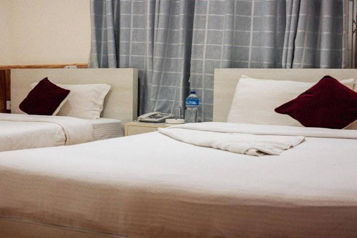 A hotel room with two beds, each with a pillow and a blanket. There is a nightstand with a phone and a bottle of water.