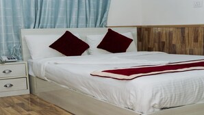 Una cama bien hecha con sábanas blancas y dos almohadas rojas, una mesita de noche con un teléfono y un cabecero de madera.