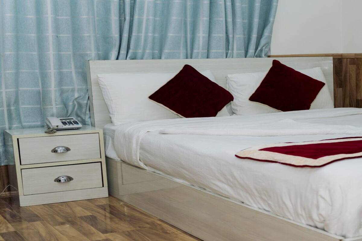 A neatly made bed with white linens and two red pillows, a bedside table with a phone, and a wooden headboard.