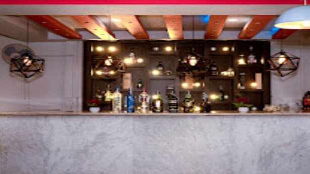 Una zona de bar con mostrador de mármol, varias botellas y luces colgantes.